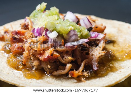 Carnitas tacos with red onion and raw salsa verde. Mexican slow cooked pork dish isolated on black plate