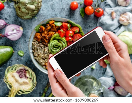 Girl's hands taking photo of Buddha bowl salad by smartphone. Healthy vegan food, clean eating, dieting, top view