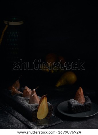Vegan brownie chocolate loaf cake with pear autumn homemade baked pastry dessert gourmet food on black background. Dark and moody style food photo. icing sugar is frozen in motion