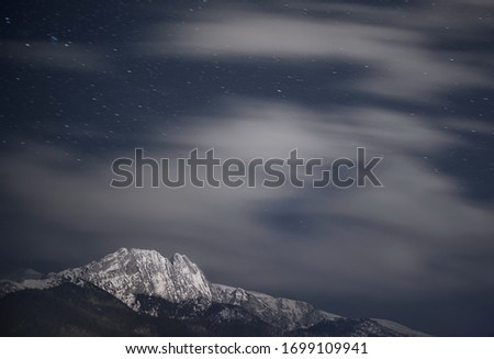 night photography of dramatic snow covered mountain Giewont with stars and clouds. Poland National Park Zakopane.