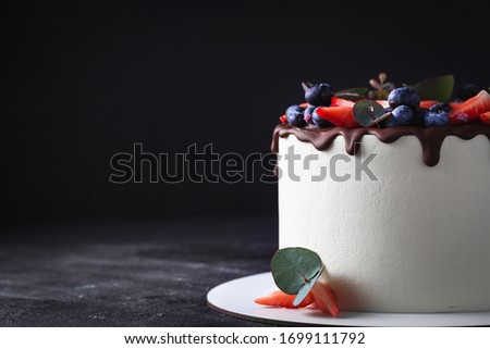 Beautiful white cake with chocolate drips, strawberries and blueberries on top. wedding or birthday cake on the black background