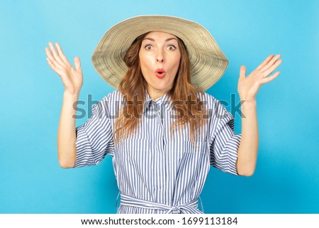 shocked young girl in a dress and hat on a blue background. Concept of vacation, summer and travel