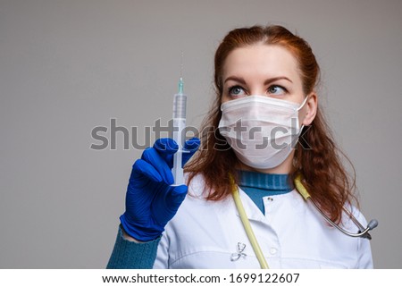 Beautiful woman doctor in white medical clothes, mask, blue gloves and phonendoscope on her shoulders, picture isolated on grey background