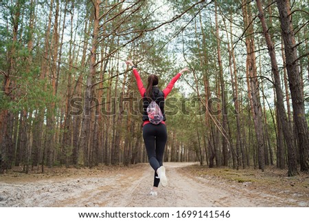 Happy girl is walking in a beautiful pine forest at the weekend. She is listening favorite music. She has a beautiful smile. Healthy lifestyle and relax concept.