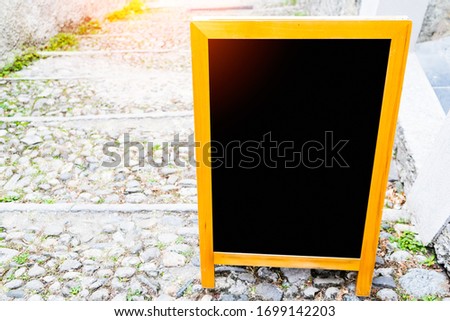 ฺBlack board wooden on the rock path way with sunlight  background.Chalkboard with space is in front of the restaurant for write recommend Menu,signature dish or time to open or close.