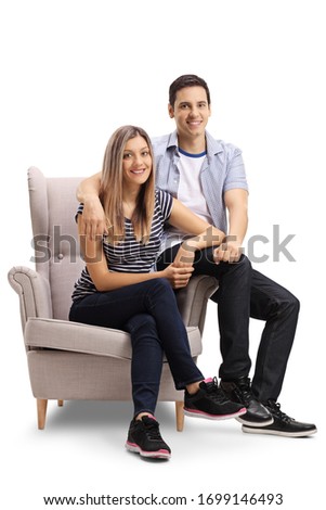 Young couple sitting in an armchair and smiling at the camera isolated on white background