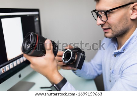 Young man change lens at his camera while sitting at the office desk