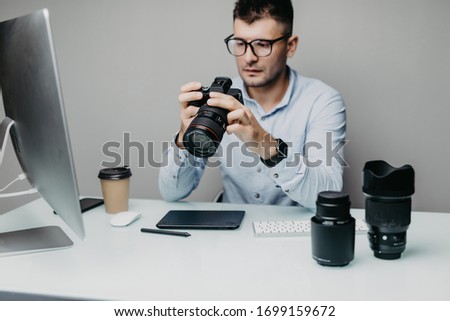 Top view serene bearded photographer watching at camera while holding it in arms in office. Image concept