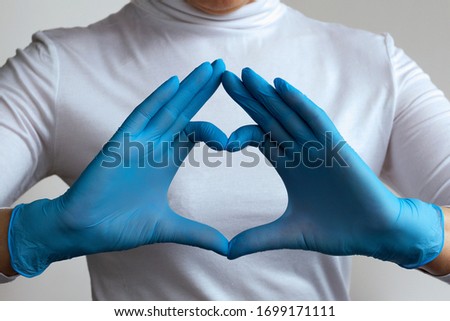 Woman doctor's hands in blue gloves form a heart shape in home. stay home. Close-up. hands in blue medical latex gloves. Hand gestures for expressing emotions. Medical healthcare.