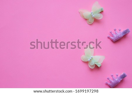 Beautiful baby hair clips in the form of yellow butterflies, with beads and a  crown, lie vertically on a pink background. Place for text, beauty and style with young, children's accessories.