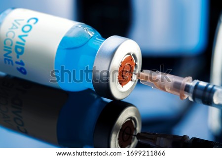 Covid-19 Written vaccine bottle with a blue liquid and taking the vaccine from it with a syringe on a laboratory like background. Royalty-Free Stock Photo #1699211866