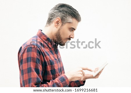Side view of focused man using tablet pc. Concentrated bearded man in checkered shirt design digital tablet on grey background. Wireless technology concept