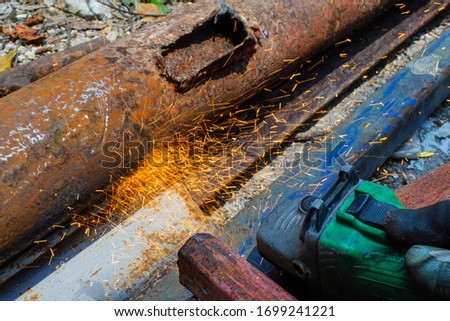 Worker finishing a steel pipe product by electric grinder. Sparks in the air.