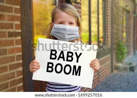 Young child girl with mask at home during the lockdown and holding a sign with the words BABY BOOM during Covid-19 Coronavirus worldwide pandemic 