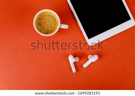 Modern communication device on touch digital tablet screen white wireless headphones coffee cup of espresso on red background