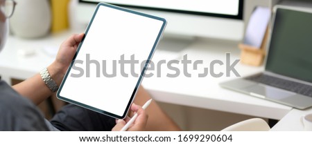 Cropped shot of male entrepreneur reading informations on vertical blank screen tablet while sitting at workspace