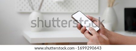Cropped shot of male freelancer working with mock-up smartphone while sitting at minimal home office 