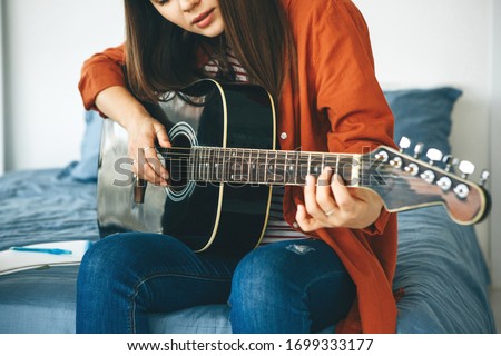 The guitarist plays the guitar. Or a girl learns to play the guitar at home. Home-based individual tuition. Royalty-Free Stock Photo #1699333177