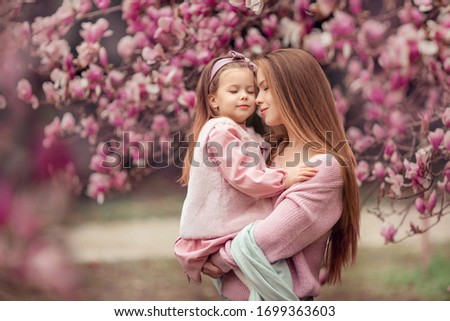 Happy family mother and daughter in pink clothes in the spring in a flowered park for a walk. woman holding a baby in her arms, they closed their eyes and dream
