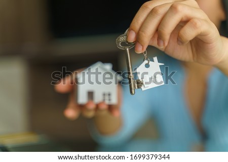 Female hand holding house key and house model.Real estate and mortgage investment.Being an easy homeowner. Royalty-Free Stock Photo #1699379344