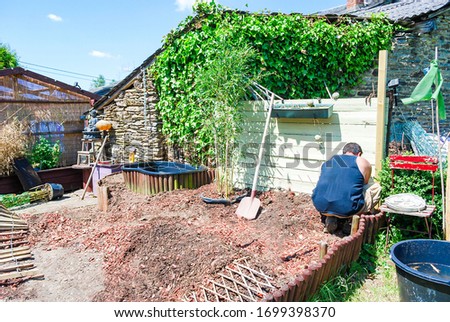 Outdoor, a man working or cleaning in garden sunny day in summer season with background dirty place, old wooden fence ,outils garden's objects, trees and blue sky and white clouds. Hobby idea
