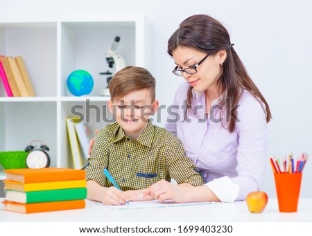 Female private tutor helping young student with homework at desk in bright child