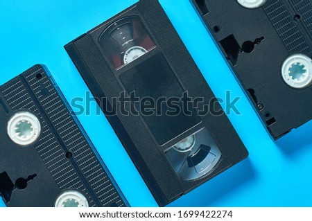 Row of black old plastic vhs video cassettes lies on blue desk. Concept of 90s. Top view. Close-up