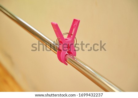 Large pink plastic clothes peg hung on a stainless steel rail in the house on a yellow wall background. Clothes pins are used to prevent clothing from falling on to surface while being sunlight.