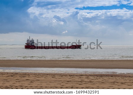 Coast and sandy beach at the North Sea in Vlissingen in the Netherlands. In the background are storm clouds and a transport ship at sea.