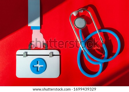 Doctor hand hold first aid kit with stethoscope on red background. World Health Day. Healthcare concept. Space for text. Soft focus. Top view.