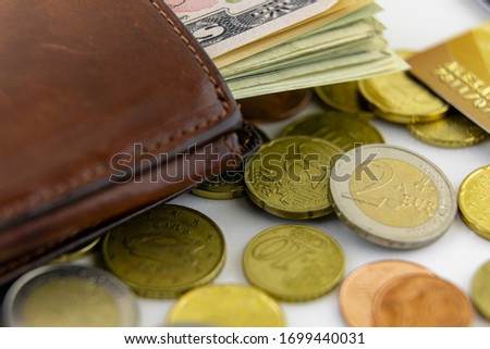 A lot of us dollar bills in a brown wallet, Euro coins and part of a gold credit card. Macro photo.