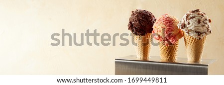 Three servings of tasty creamy ice cream in cornets with a scoop of strawberry, chocolate and Oreo or choc chip against a neutral beige gradient background with copy space in a panorama banner Royalty-Free Stock Photo #1699449811
