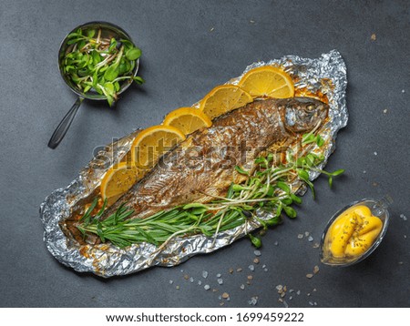 overhead view to gilled trout on foil plate with cheese sauce and green herbs