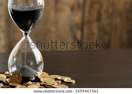 Time is money concept. Close up of hourglass with money coins Royalty-Free Stock Photo #1699467361