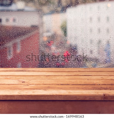 Empty wooden deck table over window with rain drops. Ready for product montage display