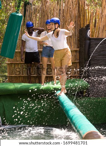 Group of people passing horizontal bar with water obstacles one by one at adventure park