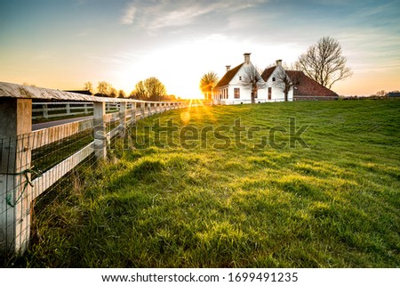 Dutch landscape with historical houses in evening along a curved road with white fence in the country - Groningen, Holland, Europe Royalty-Free Stock Photo #1699491235