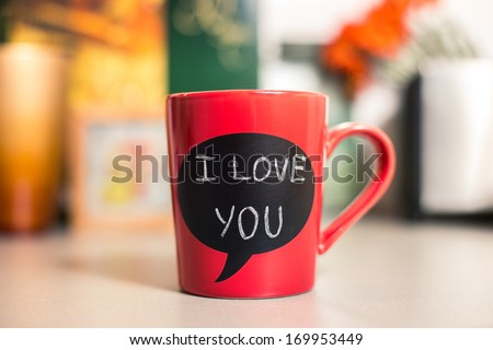 Red ceramic cup with I love you sign made with chalk. Standing on a kitchen table. 