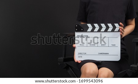 Female model's hand is holding white clap board or movie slate use in video production and movie industry on black background.