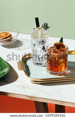Gin tonic and Negroni cocktail, with charred orange, lemon slice and blooming rosemary, on a small table. Vintage aesthetic Royalty-Free Stock Photo #1699584106