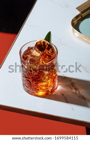 Negroni cocktail, with charred lemon and sage leaf, on a small table. Vintage aesthetic Royalty-Free Stock Photo #1699584115