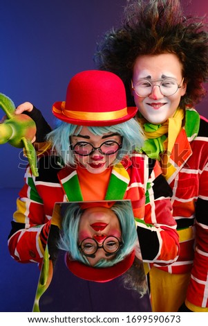 two clowns a man and a woman with bright makeup in colored costumes say they look at their reflection in the mirror. April Fools Day concept. Birthday for kids