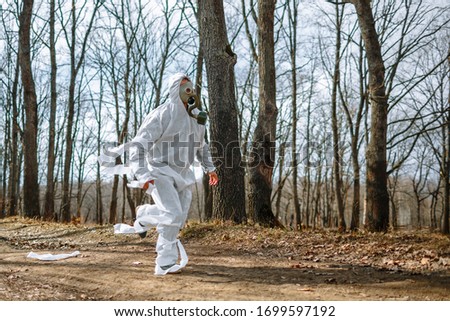 A man in a sanitary suit and a gas mask is Jogging in the woods. The suit is tied with toilet paper Royalty-Free Stock Photo #1699597192