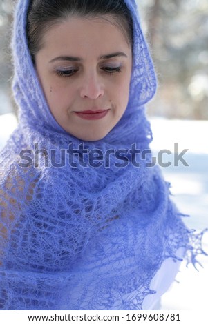 cute pretty dark-haired girl stands with her head bowed against a blurred background of a winter forest covered with a purple shawl