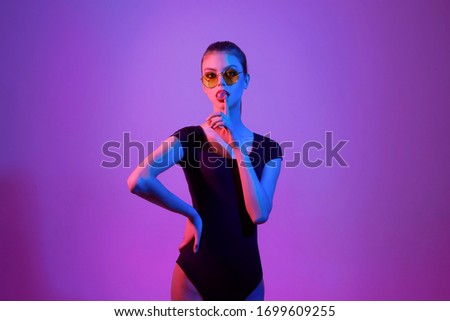 Young girl in color glasses on a pink background, chewing a gum. Colorful light