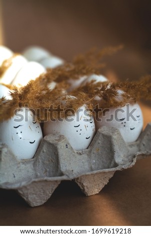 Happy Easter and white eggs in corton tray with cute faces in wreaths made of spikelets.