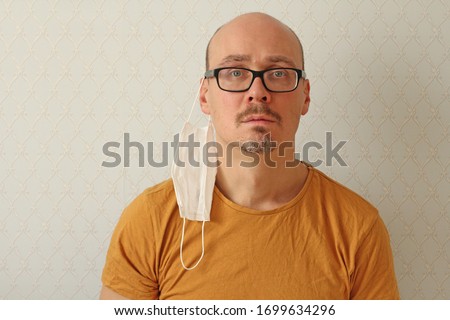 Medical bandage hangs on man’s ear. Man incorrectly puts on disposable protective medical mask in his ear protect himself from respiratory, infectious viral diseases, from coronavirus Covid - 2019. Royalty-Free Stock Photo #1699634296