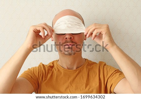 Young man incorrectly puts disposable protective white medical hygiene mask on his forehead to protect himself from respiratory, infectious viral diseases, from coronavirus. Humor, positive, fool. Royalty-Free Stock Photo #1699634302