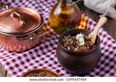 Traditional russian meal: cooked buckwheat porridge with brown butter in clay pot, served with butter, fried mushrooms, onion. Healthy food, low calories. Copper pan, wooden background, close up