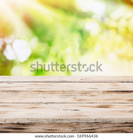 Empty rustic wooden table with golden rays of sunlight in a sunburst pattern over a blurred green country garden and bokeh suitable for product placement depicting a healthy lifestyle